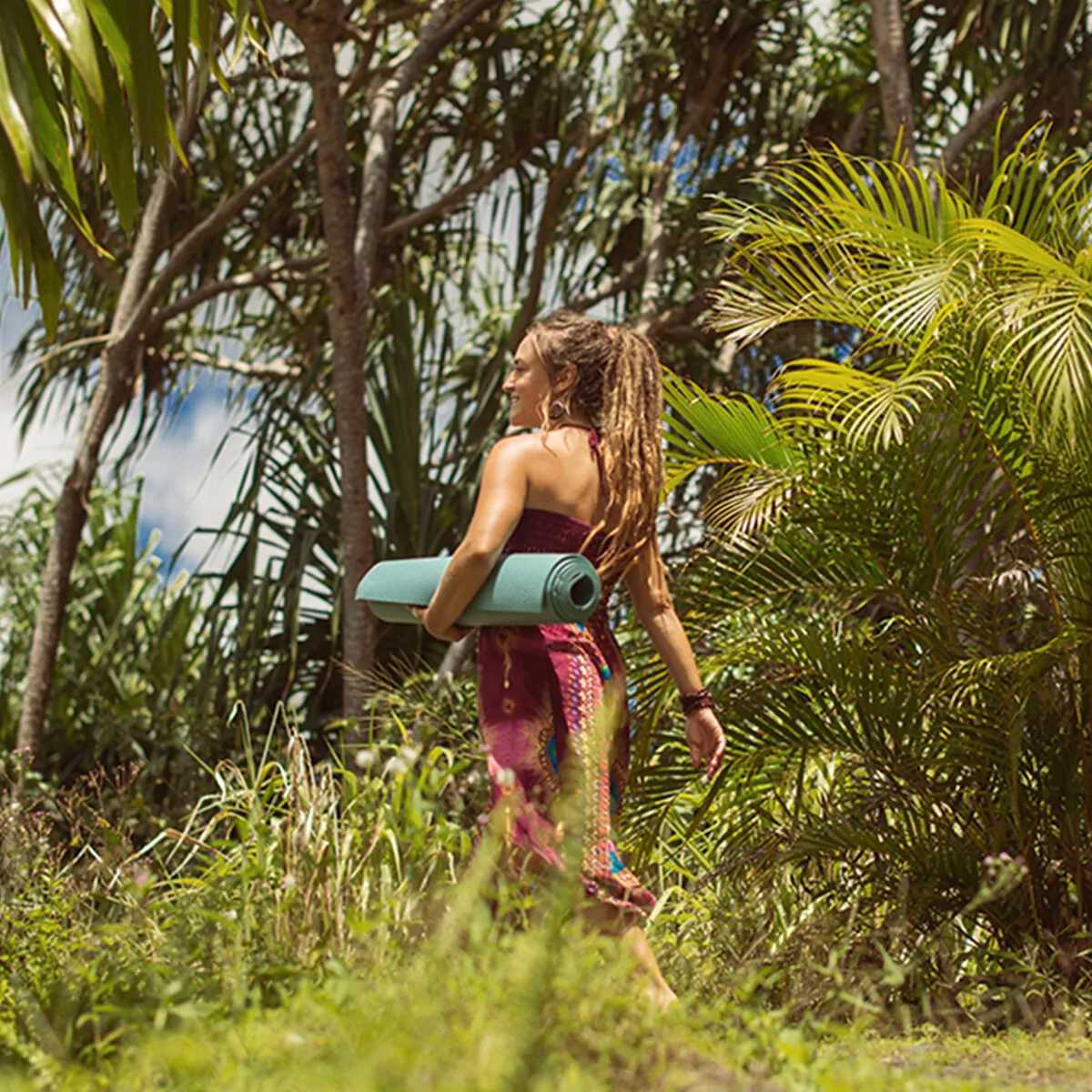A guest carrying a yoga mat through tropical greenery at KMEC